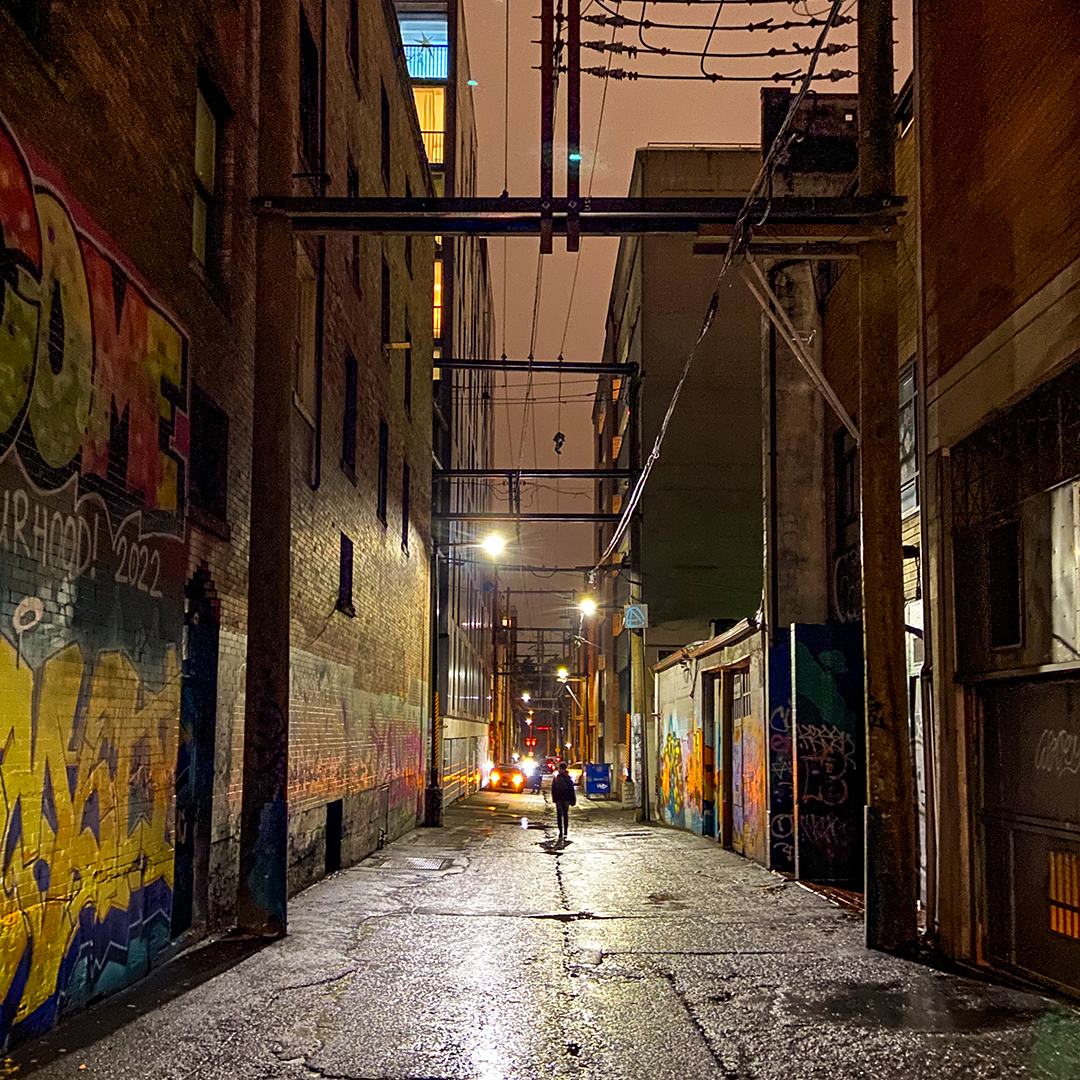 Woman walking down an alley at night.
